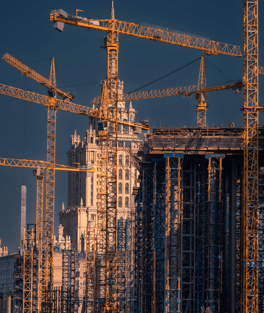 Multiple yellow tower cranes surrounding modern high-rise skyscraper construction projects in a dense city skyline.