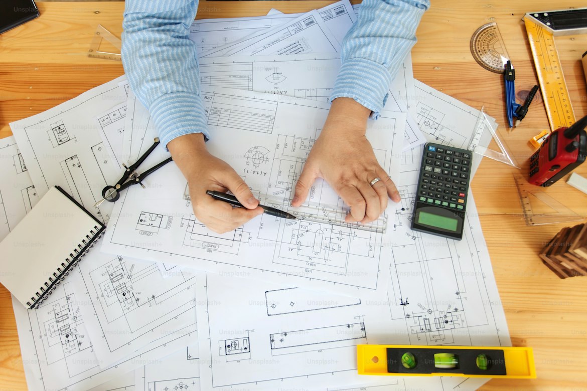 Engineer reviewing technical drawings with calculator and drafting tools.