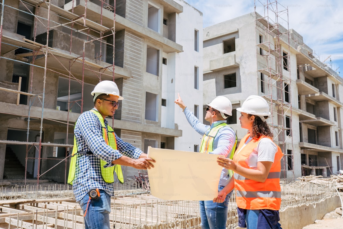 Construction team reviewing blueprints in front of a multi-storey building under construction.